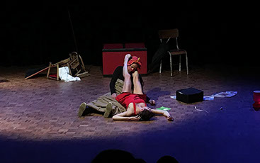 photo: le clown dort assis par terre; autour de son cou, les jambes de la danseuse qui dort elle aussi allongée par terre